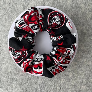 May include: Black and red patterned hair scrunchie with a white background. The pattern features stylized faces and geometric shapes.