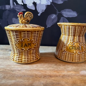 May include: A set of ceramic kitchenware in a woven basket design. The jam jar has a rooster lid and says "JAM". The creamer has a handle and says "CREAM".
