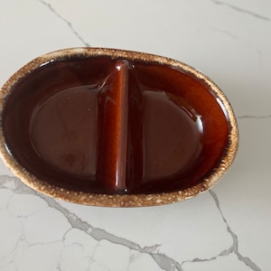 Puede incluir: Un plato de cerámica dividido en dos, de color marrón con un glaseado moteado. El plato tiene forma ovalada y tiene dos secciones.