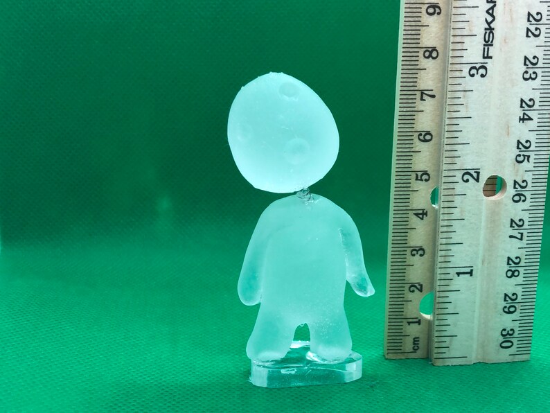 May include: A clear glass figurine of a person with a round head and a simple body shape. The figurine is about 6 inches tall and is standing on a clear plastic base.