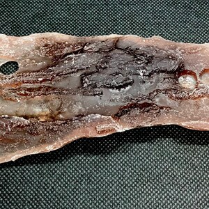 May include: A light brown, translucent, irregularly shaped piece of selenite with two holes drilled through it. The selenite has a rough, textured surface and a smooth, polished edge.