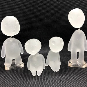 May include: Four frosted glass figurines of people with no facial features. The figurines are standing on clear plastic bases.