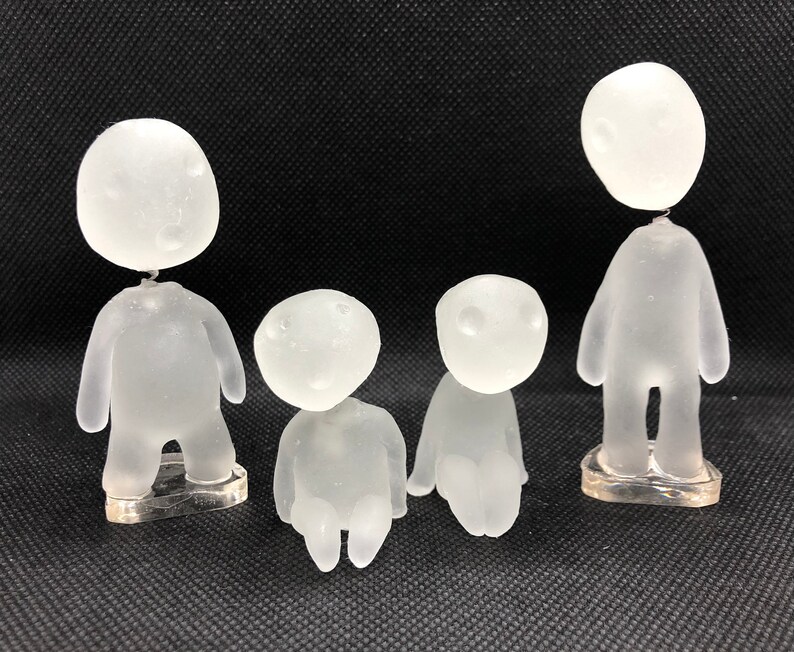 May include: Four frosted glass figurines of people with no facial features. The figurines are standing on clear plastic bases.