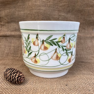 May include: White ceramic planter with a green and yellow floral design. The planter has a rounded bottom and a wide rim.