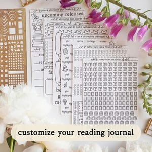 May include: A set of white sticker sheets with black line art designs for reading journals, featuring headers like upcoming releases, book awards, review trackers, and various icons including books, stars, and headphones, arranged in a layered stack.