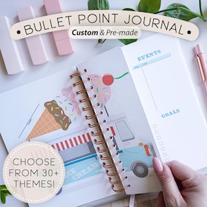 May include: Open bullet point journal with a spiral binding and a colorful ice cream theme. The journal features the text "BULLET POINT JOURNAL" and "Custom & Pre-made". The journal is open to a page with event and goal sections.
