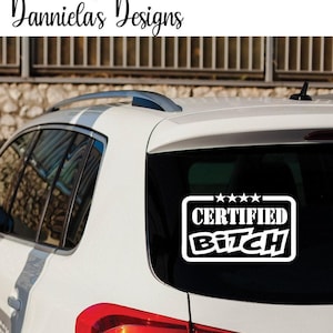 May include: White vinyl sticker with the words "CERTIFIED BITCH" in a bold, stylised font, framed by a white border and four stars. The sticker is on the rear window of a white car.