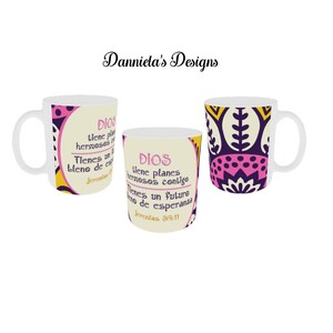 May include: Three white ceramic mugs with colorful designs. One mug features a pink and yellow pattern, another has text in Spanish, and the third has a purple and yellow floral design. The mugs are for beverages.