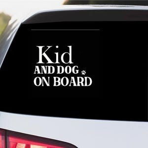 May include: A white sticker on a black car window, reading "Kid AND DOG ON BOARD". The text is in a bold, sans-serif font, with a paw print graphic. The sticker is affixed to the rear window of a vehicle.