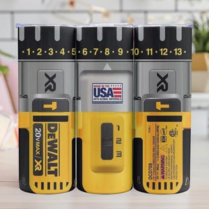 May include: Three tumblers with a design resembling a DeWalt drill. The tumblers are black, gray, and yellow, with the DeWalt and XR logos. The tumblers have a scale from 1 to 13 on the top.