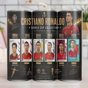 May include: A cylindrical tumbler featuring a black background with gold text reading Cristiano Ronaldo World Cup Collection. It displays six portrait panels of the athlete in a red jersey, representing years from 2006 to 2026, with Panini logos and stats.