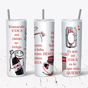 May include: White tumbler with a silver straw featuring humorous text and cartoon illustrations related to Coca-Cola. The design includes a bottle and a can of Coke, with text in Spanish. A fun, novelty item.