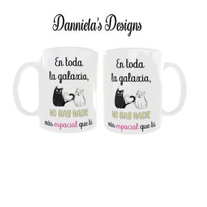 Könnte beinhalten: Zwei weiße Keramikbecher mit einem Design aus schwarzen und weißen Katzen. Auf den Bechern steht der Text "En toda la galaxia, NO HAY NADIE más espacial que tú". Die Becher sind von Danniela's Designs.