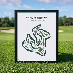 Op de afbeelding: Een ingelijste print met een gestileerde kaart van de Sequoyah National Golf Club in North Carolina. Het kunstwerk toont donkergroene fairways, lichtgroene roughs en blauwe waterhindernissen op een witte achtergrond, in een zwarte lijst.