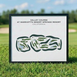 Può includere: Stampa incorniciata del Valley Course al Marriott's Desert Springs Resort in California. L'opera presenta un layout del campo da golf verde e blu su sfondo bianco, con testo in alto. La cornice è nera e la stampa è esposta sull'erba.