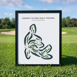 May include: Framed print of the Desert Dunes Golf Course in California. The course layout is shown in green and blue on a white background, framed in black. The print is displayed on a green grassy surface under a blue sky.