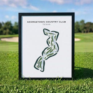 May include: A framed print featuring a stylized map of the Georgetown Country Club in Texas. The artwork displays a dark green golf course layout on a white background with a light blue path, all enclosed within a simple black frame.
