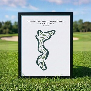 May include: A framed print of the Comanche Trail Municipal Golf Course in Texas. The print features a green and white golf course layout against a white background. The frame is black, and the print is displayed on a grassy surface.