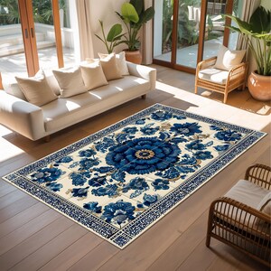Pu&ograve; includere: Un tappeto rettangolare con sfondo color crema e un grande medaglione floreale blu scuro al centro. Il design presenta intricati motivi floreali in blu e oro, rifinito con un bordo geometrico dettagliato nei colori blu e bianco.