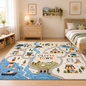 May include: A rectangular area rug featuring a colorful illustrated town map with roads, a blue river, a lighthouse, a ship, farm animals, and buildings. The center of the rug displays the text OLIVIA TOWN in a clear, bold, dark-colored font.