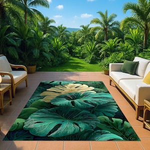 Könnte beinhalten: Rechteckiger Outdoor-Teppich mit tropischem Blattmuster in Grün und Gold. Der Teppich liegt auf einer gefliesten Terrasse, mit einem grünen Garten und Sitzgelegenheiten im Hintergrund. Dschungel-Thema.