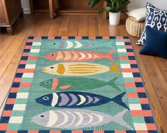 Puede incluir: Una alfombra colorida con un borde azul, verde y naranja. La alfombra presenta cinco peces estilizados en tonos de azul, verde, naranja y amarillo sobre un fondo turquesa.