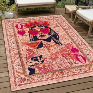May include: A pink and red rug featuring a Queen of Hearts design. The Queen is wearing a crown and sunglasses and holding a martini glass. The rug has a floral pattern and a gold border.