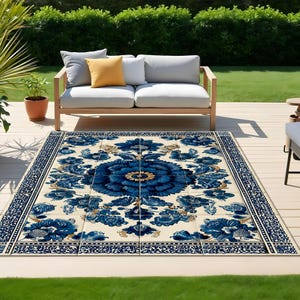 Puede incluir: Alfombra rectangular para exteriores con un diseño floral azul y dorado. La alfombra está colocada sobre una terraza de madera, con un sofá blanco y cojines en el fondo. Dimensiones aproximadas: 244 cm x 305 cm.