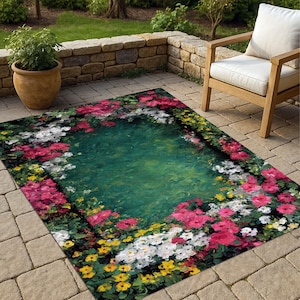 Può includere: Tappeto rettangolare da esterno con un design floreale. Fiori rosa, bianchi e gialli incorniciano un centro verde. Il tappeto è posizionato su un patio in pietra, con una pianta in vaso e una sedia di legno visibili.