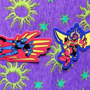 May include: Two colorful stickers featuring cartoon characters. One is a blue and black figure with red and yellow accents, the other is a red and yellow figure with blue accents. The background is purple with green sun and star patterns.