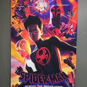 May include: A colorful poster for the movie "Spider-Man: Across the Spider-Verse" featuring Miles Morales and Gwen Stacy. The poster has a red spider symbol and the movie title. The release date is June 2.