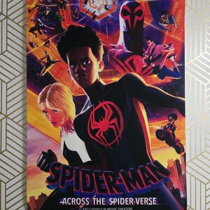 May include: A movie poster for "Spider-Man: Across the Spider-Verse" featuring Miles Morales in a black and red suit with a spider emblem. The poster has a vibrant, colorful design with multiple Spider-Man characters and the text "SPIDER-MAN" and "ACROSS THE SPIDER-VERSE".