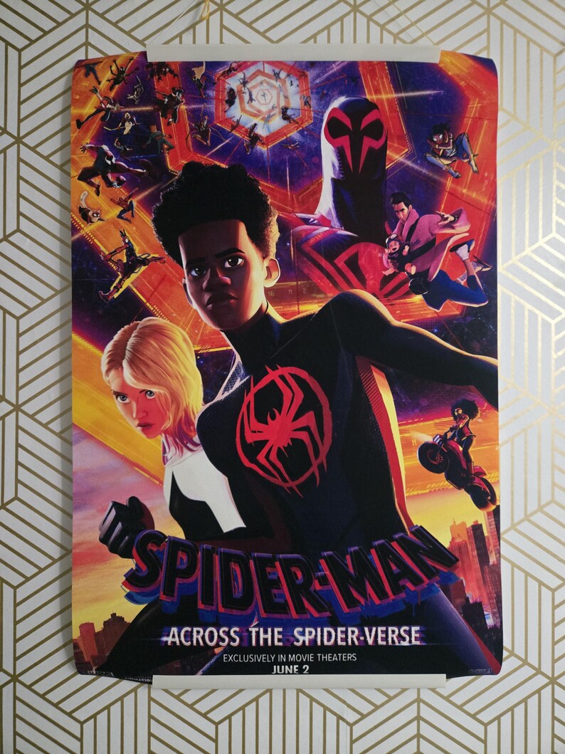 May include: A movie poster for "Spider-Man: Across the Spider-Verse" featuring Miles Morales in a black and red suit with a spider emblem. The poster has a vibrant, colorful design with multiple Spider-Man characters and the text "SPIDER-MAN" and "ACROSS THE SPIDER-VERSE".