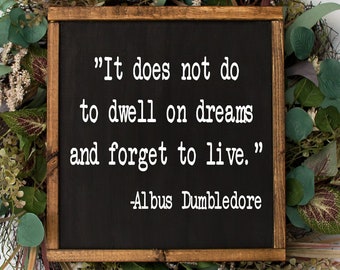 Puede incluir: Un letrero de pizarra negra con marco de madera rodeado de una corona floral verde. El letrero dice "No sirve de nada vivir en sueños y olvidarse de vivir." -Albus Dumbledore