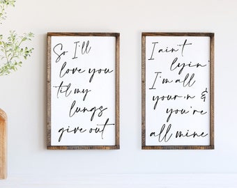 May include: Two wooden signs with black calligraphy. The left sign reads "So I'll love you til my lungs give out". The right sign reads "I ain't lyin I'm all your'n & you're all mine".