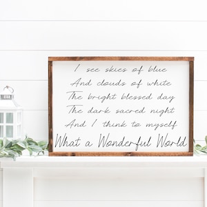 May include: A framed wooden sign with the quote "I see skies of blue... What a Wonderful World" in black script. The sign is displayed on a white mantel with a white lantern and greenery.
