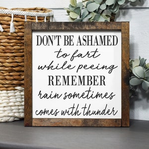 May include: A wooden sign with the text "Don't be ashamed to fart while peeing. Remember rain sometimes comes with thunder." The sign is brown with a white background and black text.