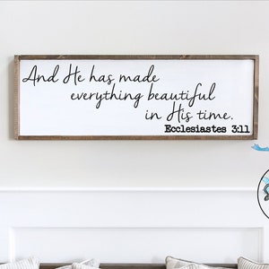 May include: A wooden sign with a white background and black text that reads "And He has made everything beautiful in His time. Ecclesiastes 3:11". The sign is hanging on a white wall above a wooden bench with gray and white striped pillows.
