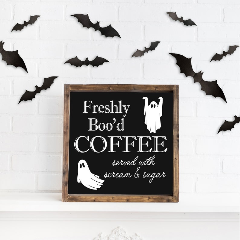 K&ouml;nnte beinhalten: Ein schwarzes Schild aus Schiefer mit einem Holzrahmen tr&auml;gt die Aufschrift "Freshly Boo'd COFFEE served with scream & sugar". Zwei wei&szlig;e Geister-Silhouetten befinden sich auf dem Schild. Das Schild h&auml;ngt an einer wei&szlig;en Backsteinwand, an der schwarze Flederm&auml;use h&auml;ngen.