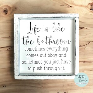 May include: White framed sign with the text "Life is like the bathroom, sometimes everything comes out okay and sometimes you just have to push through it." The sign is a custom home decor item.