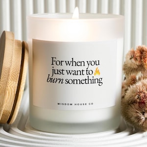 May include: A white candle in a frosted glass jar with a wooden lid. The label reads "For when you just want to burn something" with a flame graphic. The brand name "Wisdom House Co" is at the bottom.