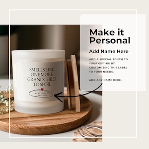 Pu&ograve; includere: Una candela bianca con la scritta "SMELLS LIKE ONE MORE GRANDCHILD TO SPOIL" e "BABY WILSON EST. 2026". La candela &egrave; su un vassoio di legno con un coperchio di legno. L'immagine include anche il testo "Make it Personal".