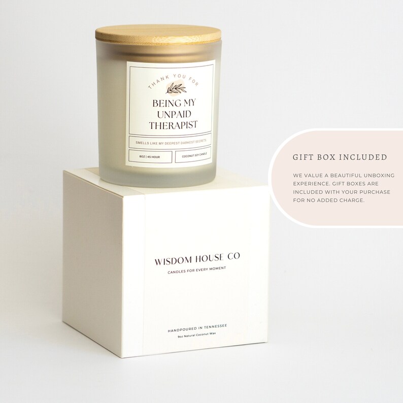 May include: White candle with a wooden lid and a label that reads "Thank you for being my unpaid therapist". The candle is on a white box with the text "Wisdom House Co. Candles for every moment" and "Handpoured in Tennessee Soy Natural Coconut Wax". The text "Gift Box Included" is in the upper right corner of the image. The text below reads "We value a beautiful unboxing experience. Gift boxes are included with your purchase for no added charge."