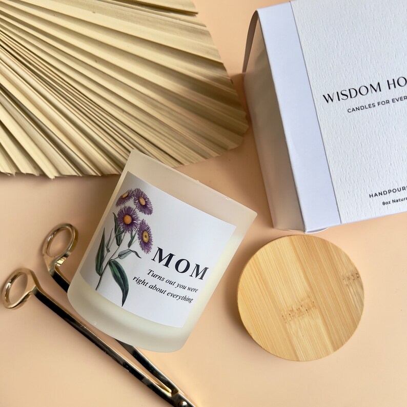 May include: A white candle jar with a floral design and the text "MOM Turns out you were right about everything". The candle jar is on a light brown surface with a wooden lid and a gold pair of scissors.