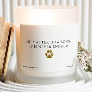 May include: A frosted glass candle with a white label featuring the text "NO MATTER HOW LONG, IT IS NEVER ENOUGH" and a paw print. The candle is in a white holder with a wooden accessory and white flowers.