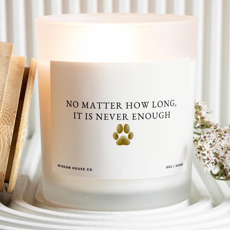 May include: A frosted glass candle with a white label featuring the text "NO MATTER HOW LONG, IT IS NEVER ENOUGH" and a paw print. The candle is in a white holder with a wooden accessory and white flowers.