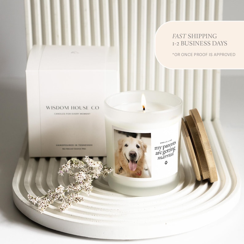 May include: A burning candle in a glass jar with a wooden lid, displaying a photo of a golden retriever and the text "my parents are getting married." A white box with the text "WISDOM HOUSE CO" is behind the candle.