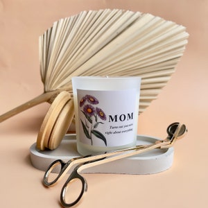 May include: A white candle with a floral design and the text "MOM Turns out you were right about everything". The candle is on a white surface with a gold candle snuffer and a wooden coaster.