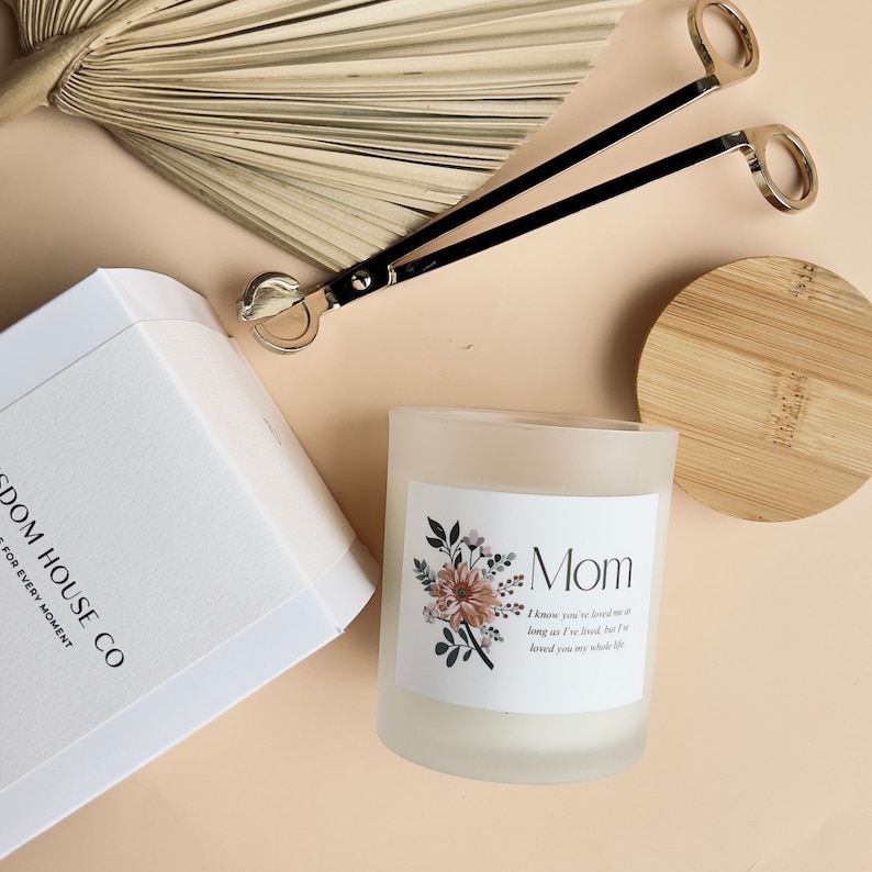 May include: A white frosted glass candle with a floral design and the word "Mom" on the label. The label also includes the text "I know you've loved me as long as I've lived, but I've loved you my whole life".