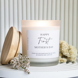 Puede incluir: Vela de vidrio blanco esmerilado con tapa de madera. La etiqueta dice "HAPPY First MOTHER'S DAY" y "THANK YOU FOR EVERYTHING YOU DO. YOU'RE AN AMAZING MOM. LOVE, GIGI".